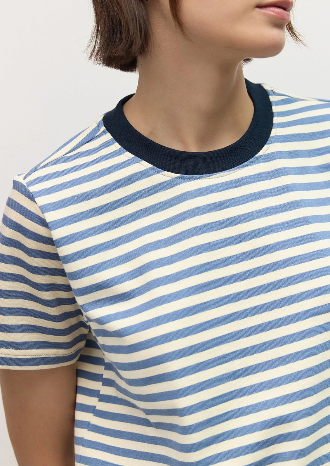 Close-up of a person wearing a short-sleeve crew-neck T-shirt with horizontal blue and off-white stripes and a dark navy ribbed collar.
