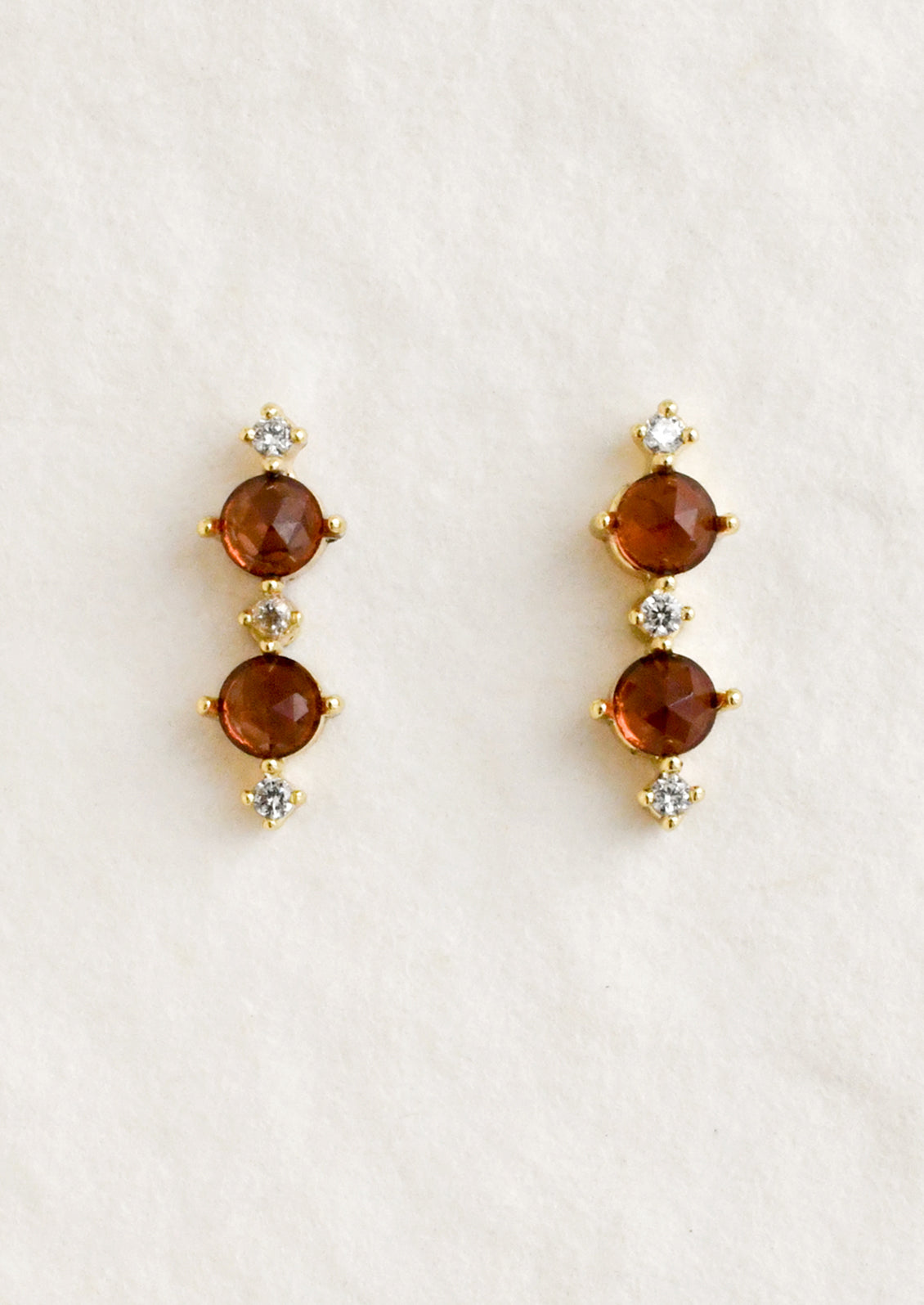 A pair of stud earrings with two garnet stones between smaller cubic zirconia stones.