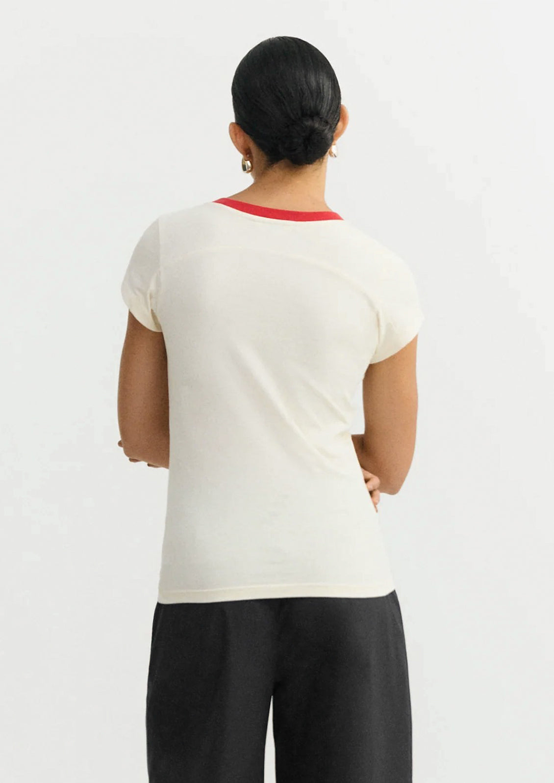 Person wearing a white top with a red neckline on a plain background