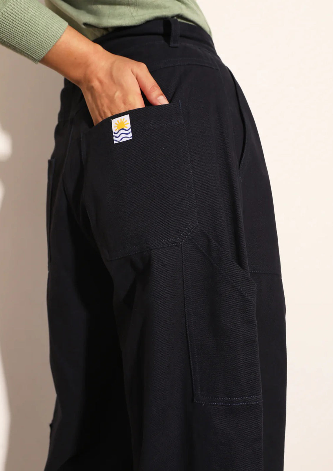 Black pants with a brand logo on the pocket against a neutral background