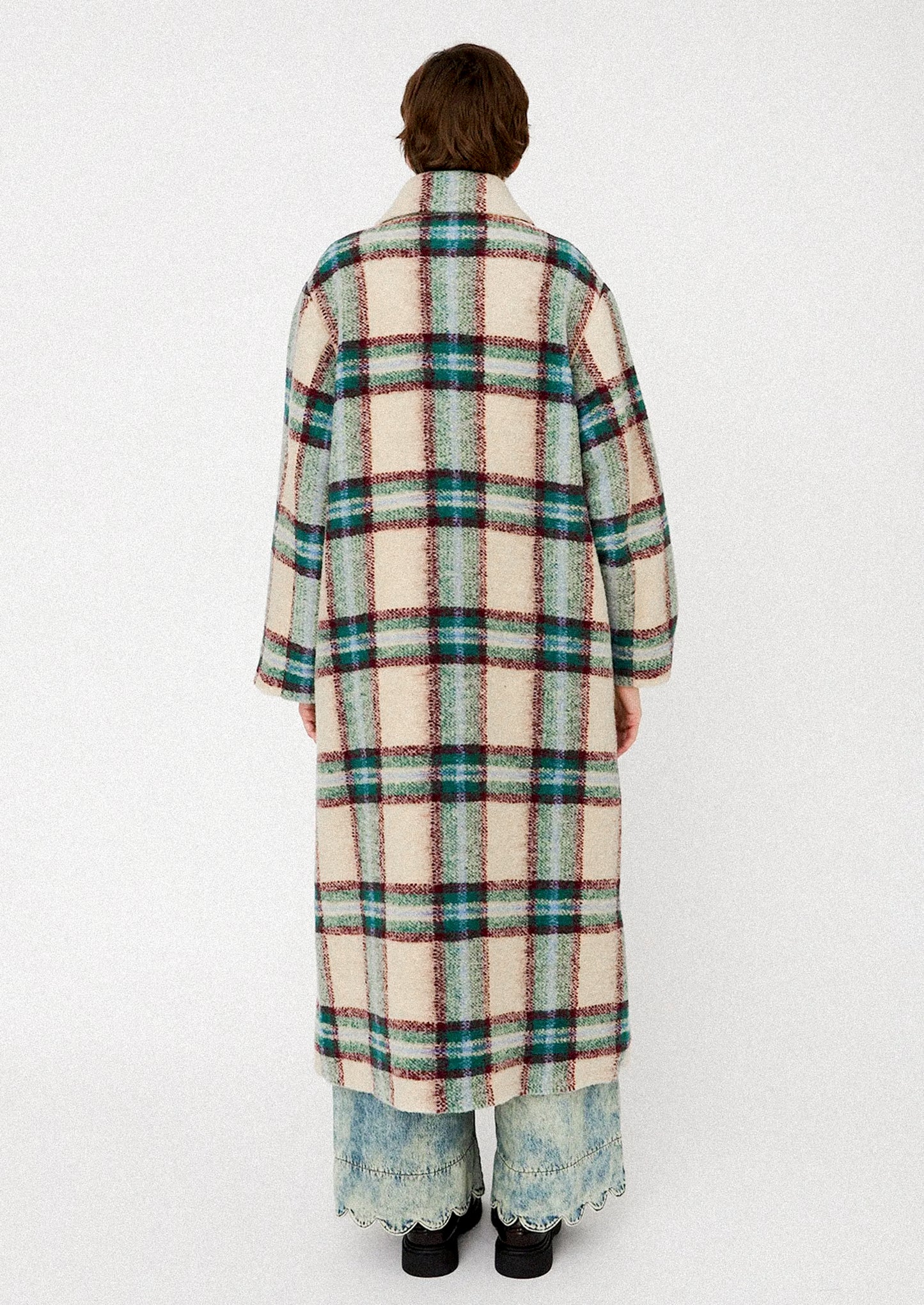 Person wearing a long plaid coat on a white background