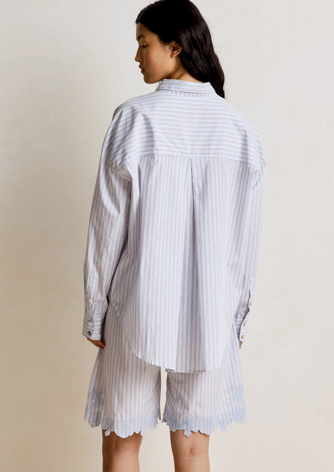 Person wearing a light blue striped shirt and shorts on a plain background