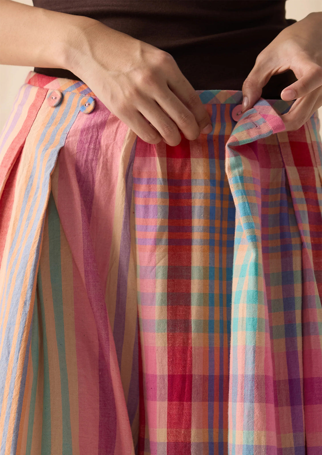Close-up of a person wearing a colorful striped and plaid skirt, adjusting the waistband with both hands.