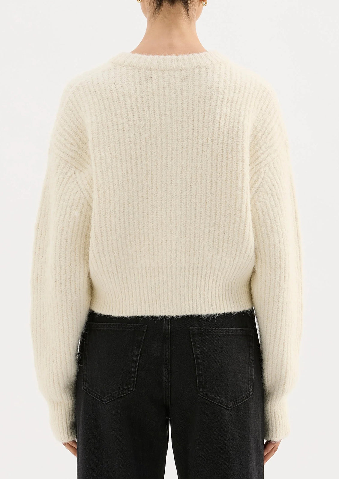 Person wearing a cream sweater and black pants on a white background