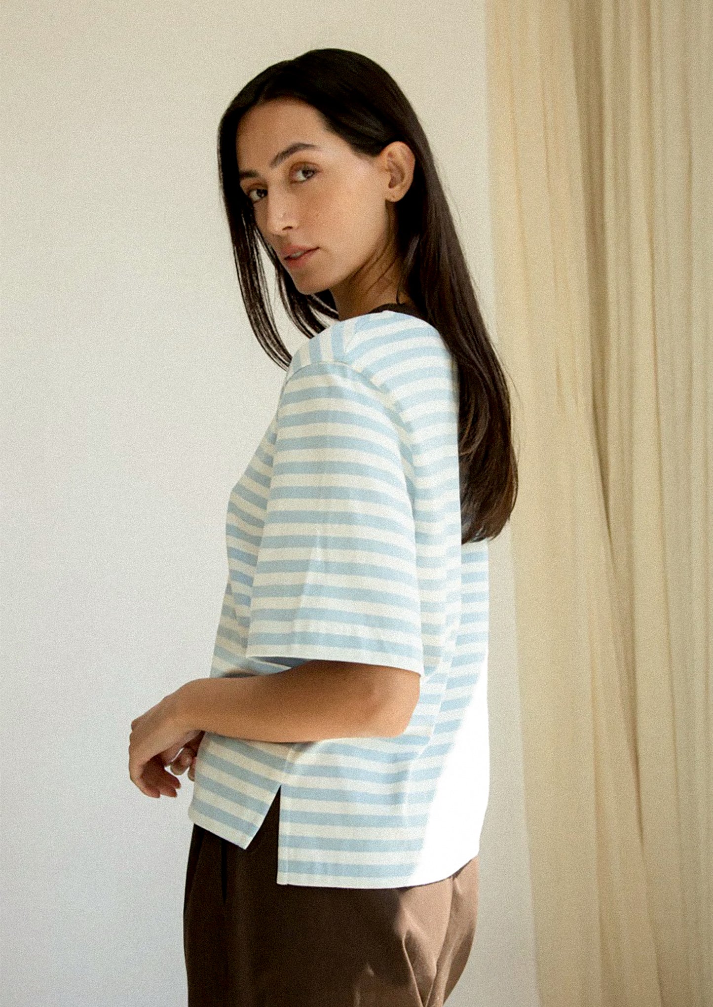 Woman wearing a light blue and white striped shirt against a neutral background