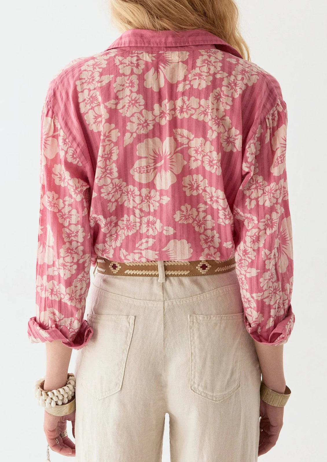 A person wearing a pink cotton shirt with tonal pinstripes and Hawaiian floral pattern.