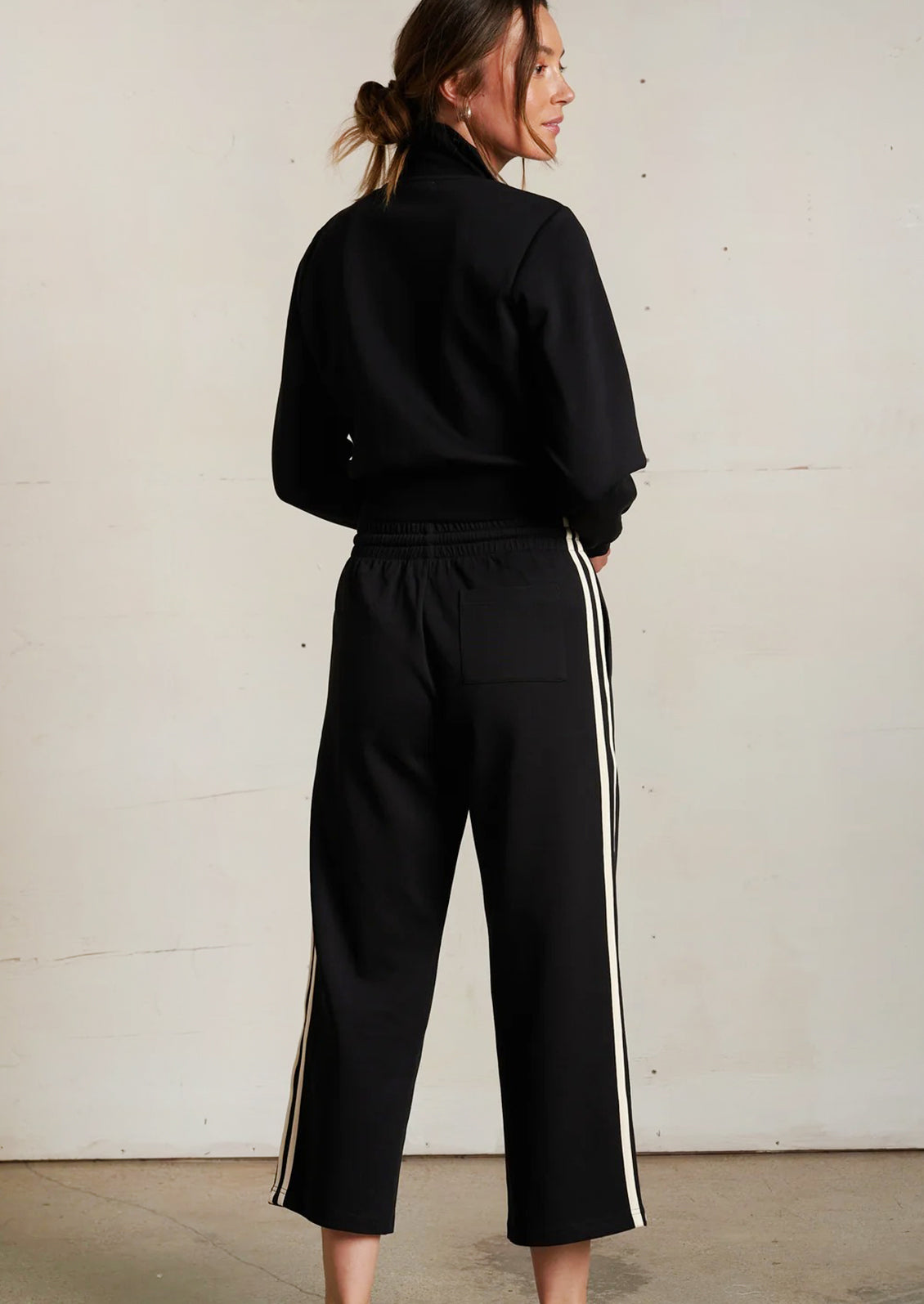 Person wearing a black tracksuit with white stripes on a plain background