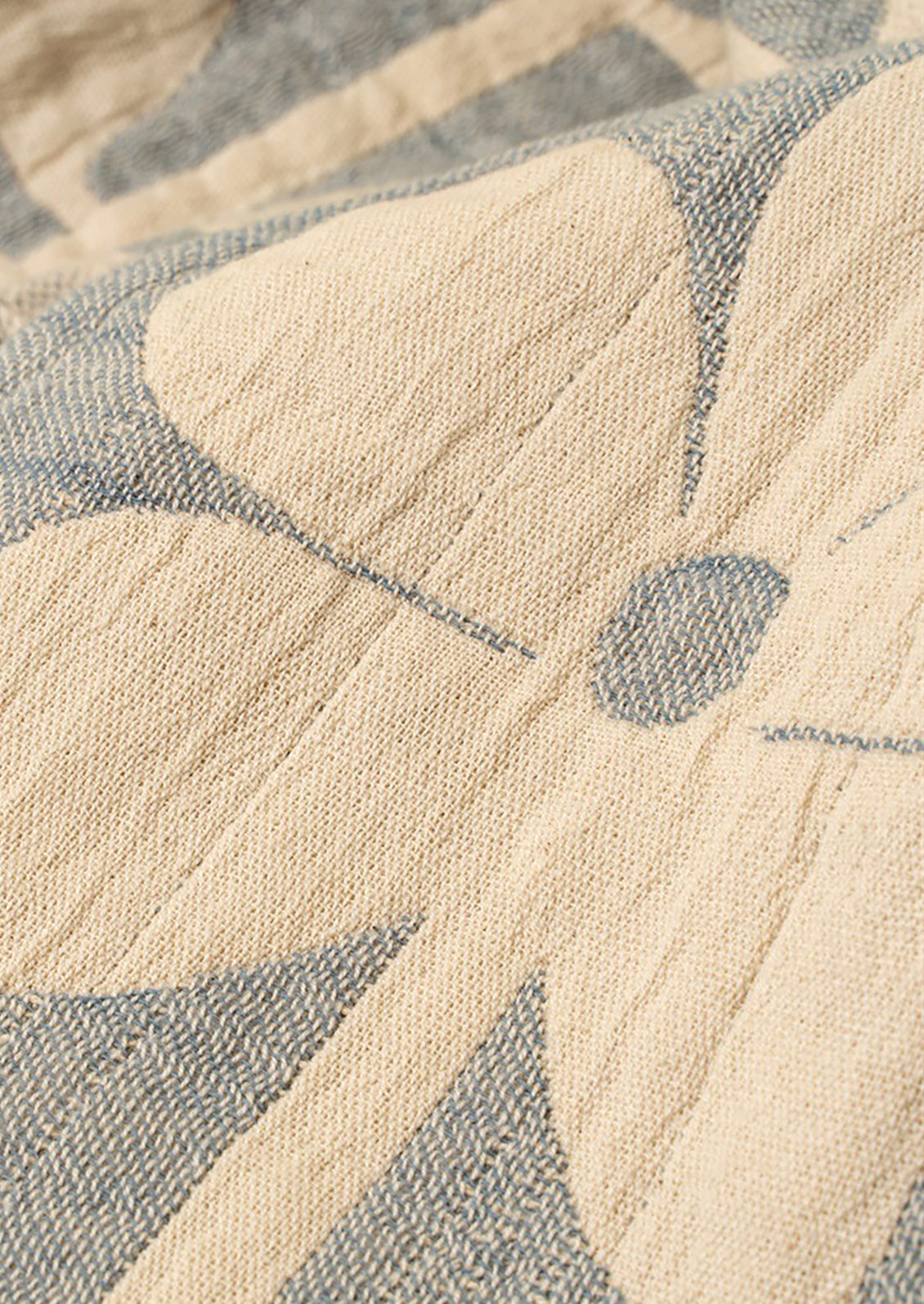 Close-up of a textured fabric with leaf pattern in beige and gray.