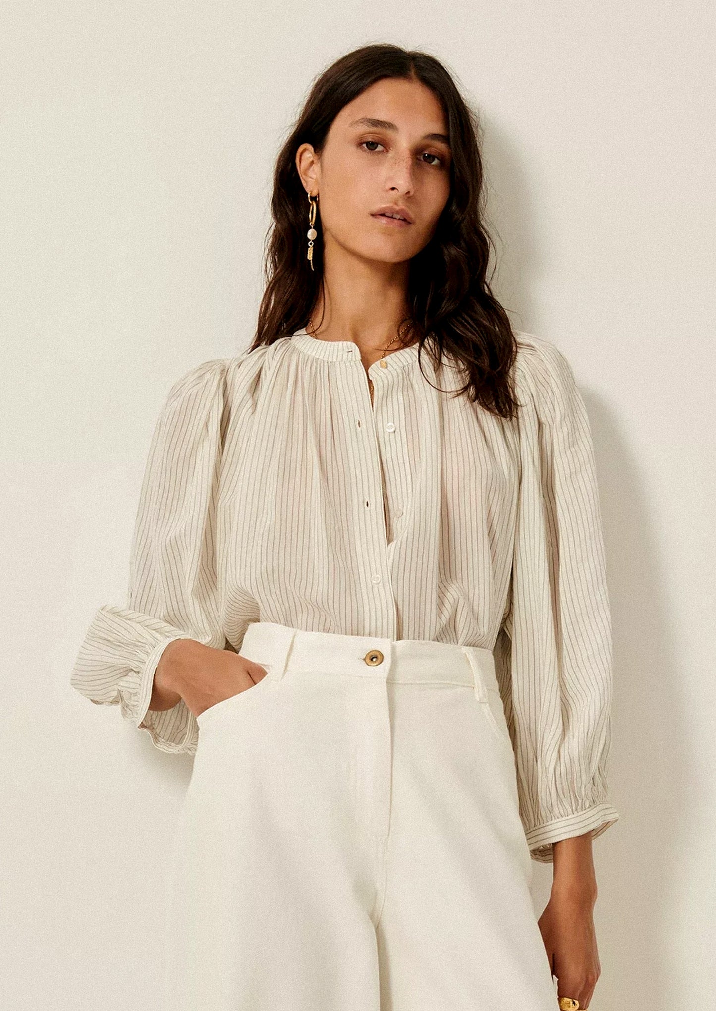 A woman wearing a white blouse with black pinstripe pattern, and cutout detailing on sleeves.