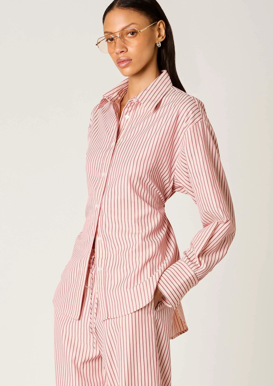 Woman wearing a pink and white striped shirt and pants on a plain background