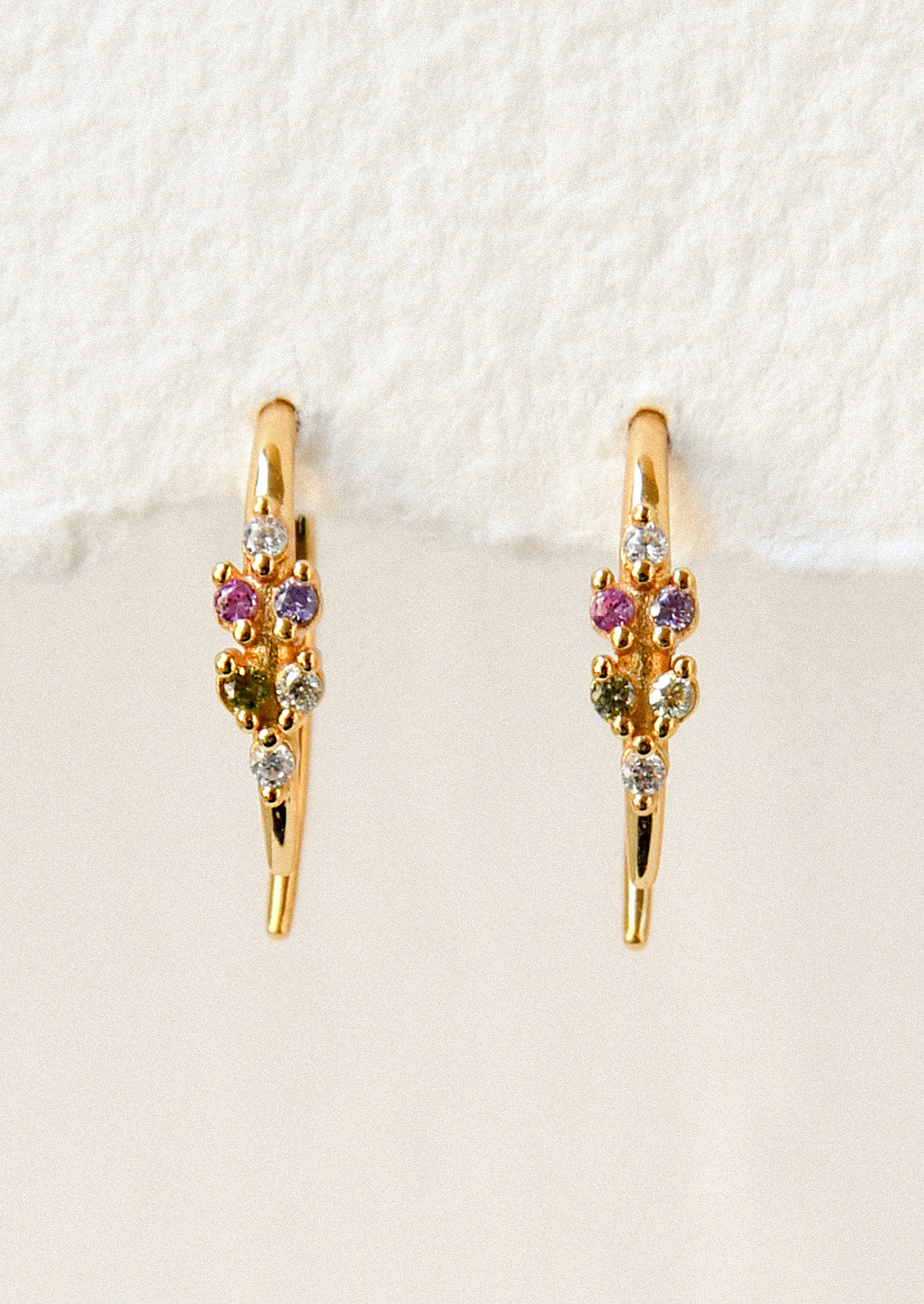 A pair of gold open hoop earrings with various colored glass stones adorned on the front.