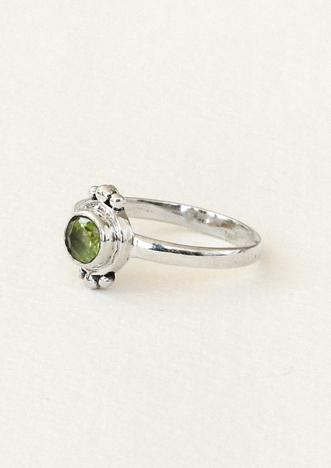 Side view of a sterling silver ring with a unique design featuring three tiny spheres on the top and bottom and a peridot gem in the center.
