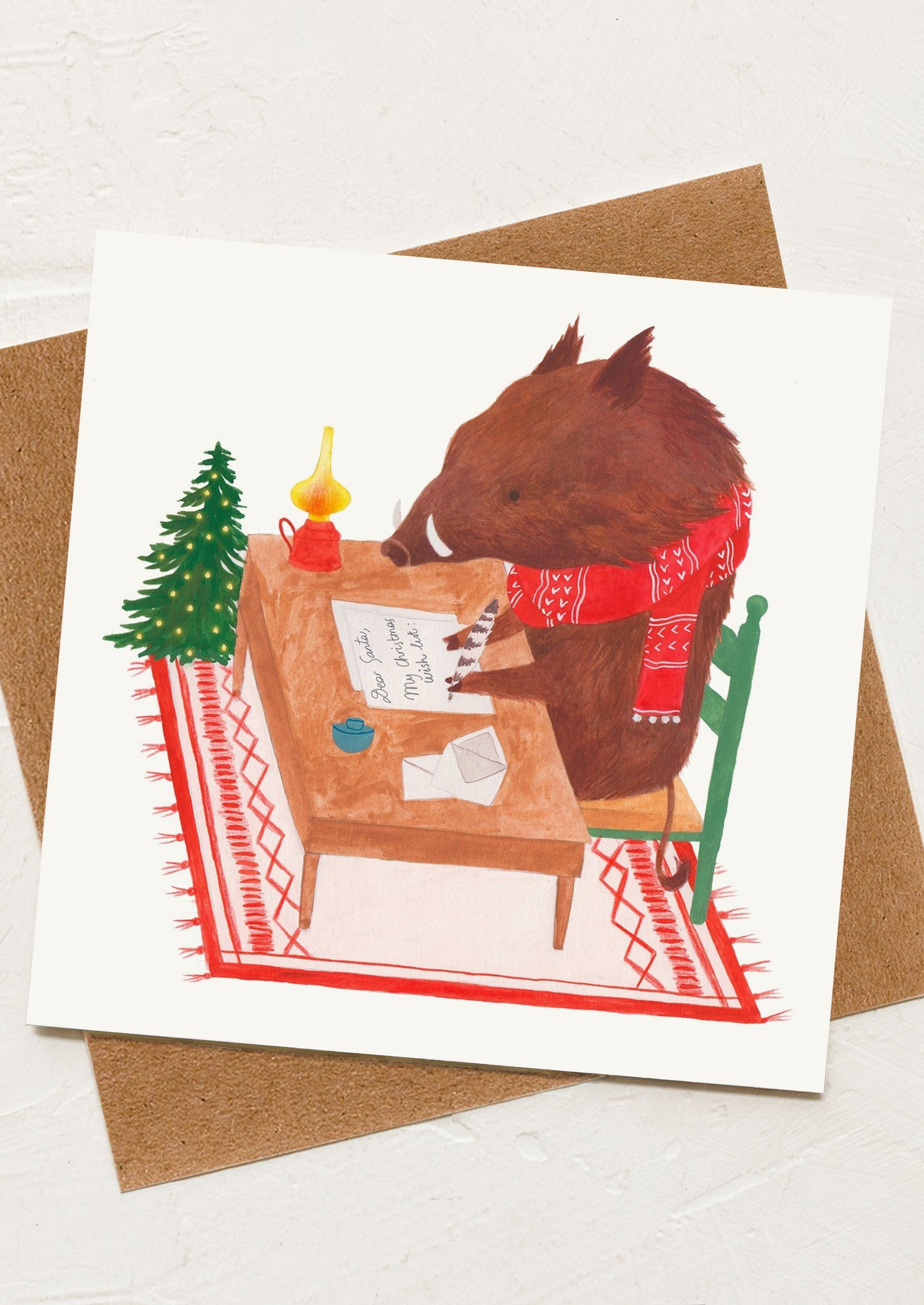 A greeting card with an illustration of a warthog writing a letter to santa.