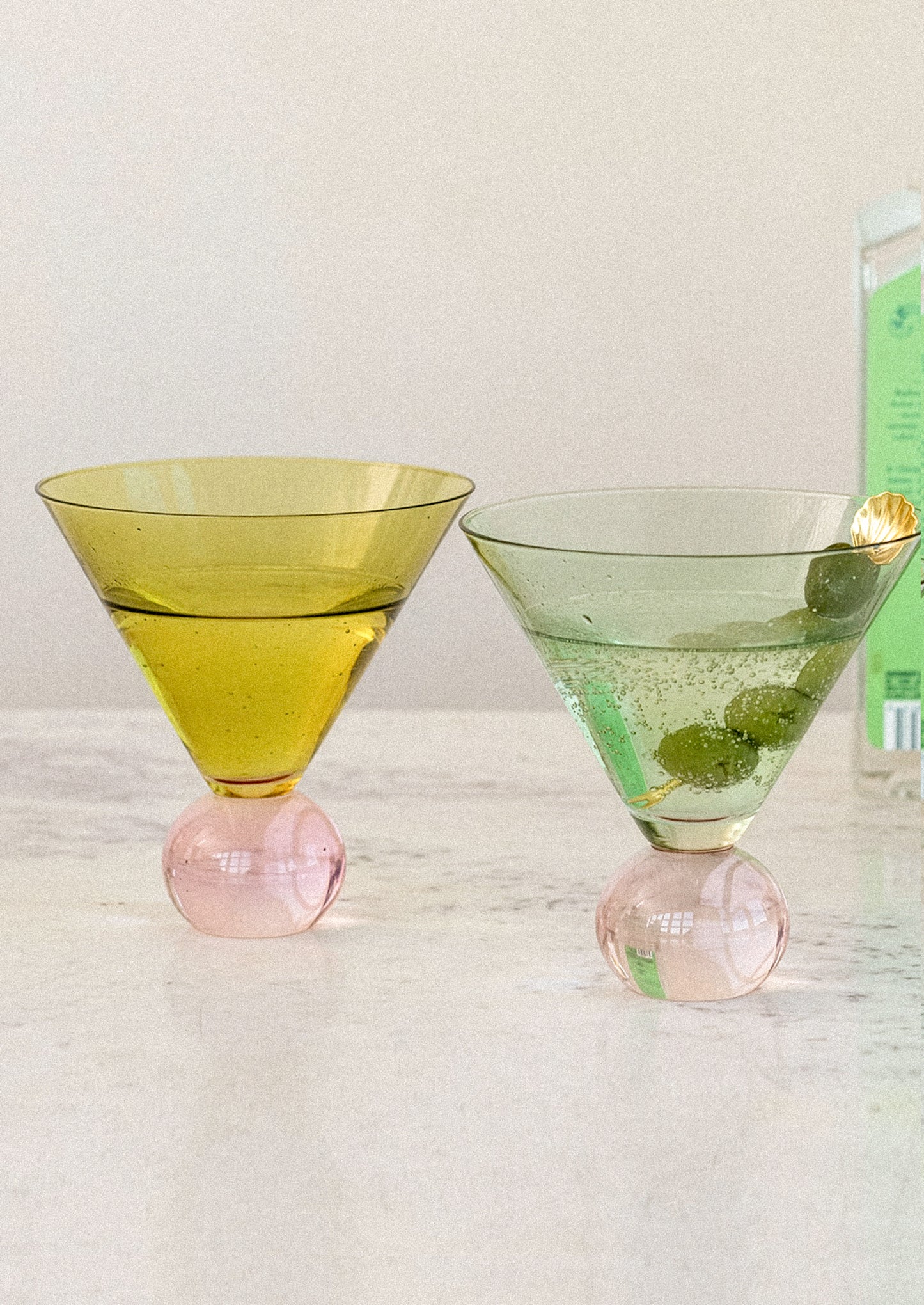 Two green cocktail glasses with pink bases on a light surface.