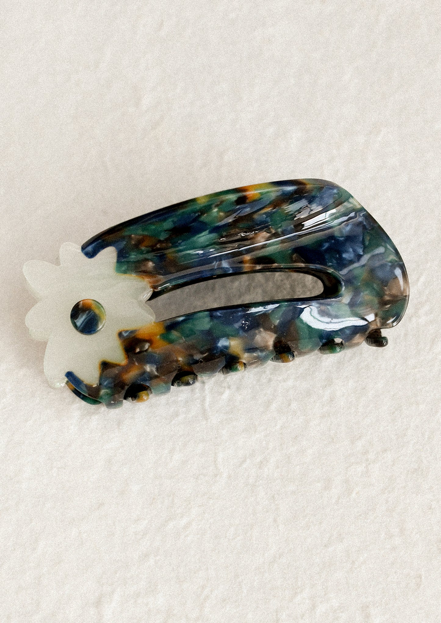 A hair claw in dark brown and blue marbleized with white flower at end.