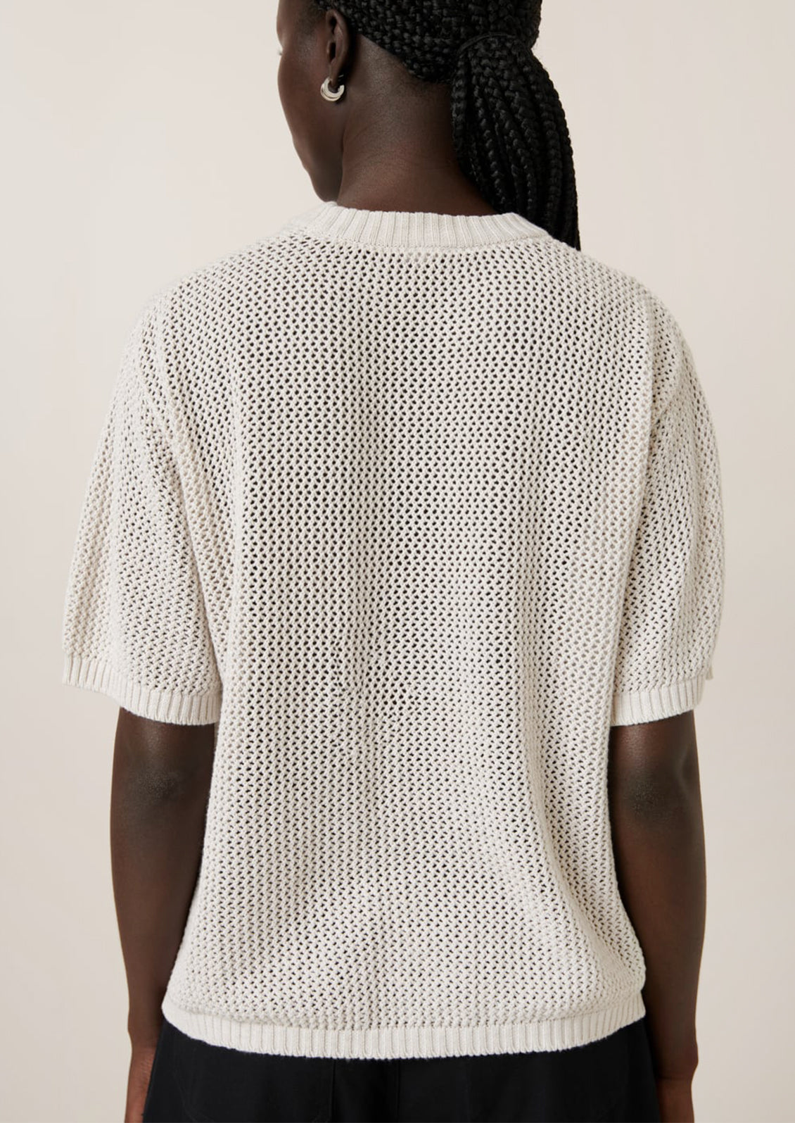 A woman wearing an open mesh knit short sleeve sweater with tonal floral motif.