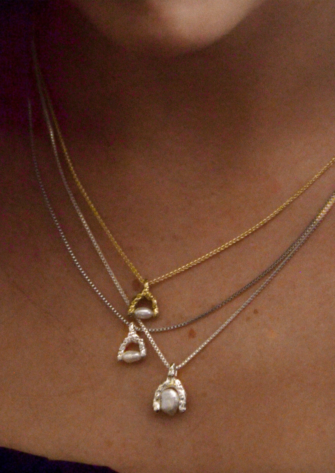 A woman wearing various chain necklaces with wishbone-shaped charms that have a keshi pearl in the center of them.