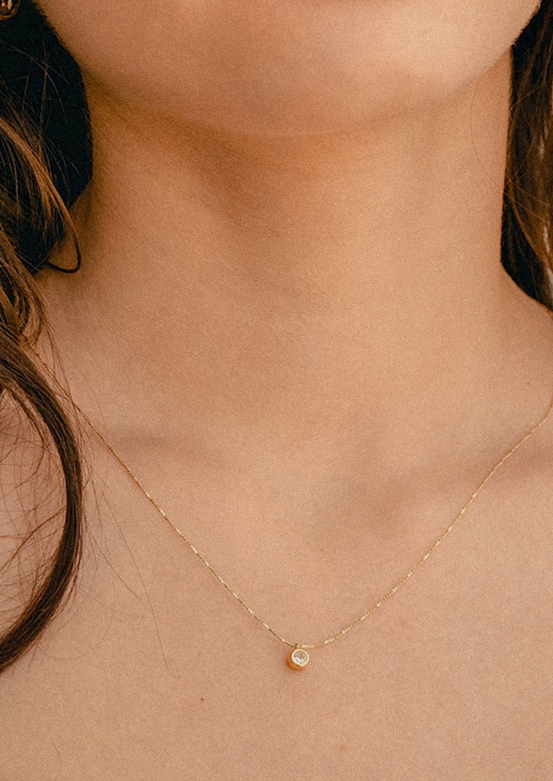 A woman wearing a simple gold necklace with a small crystal charm.