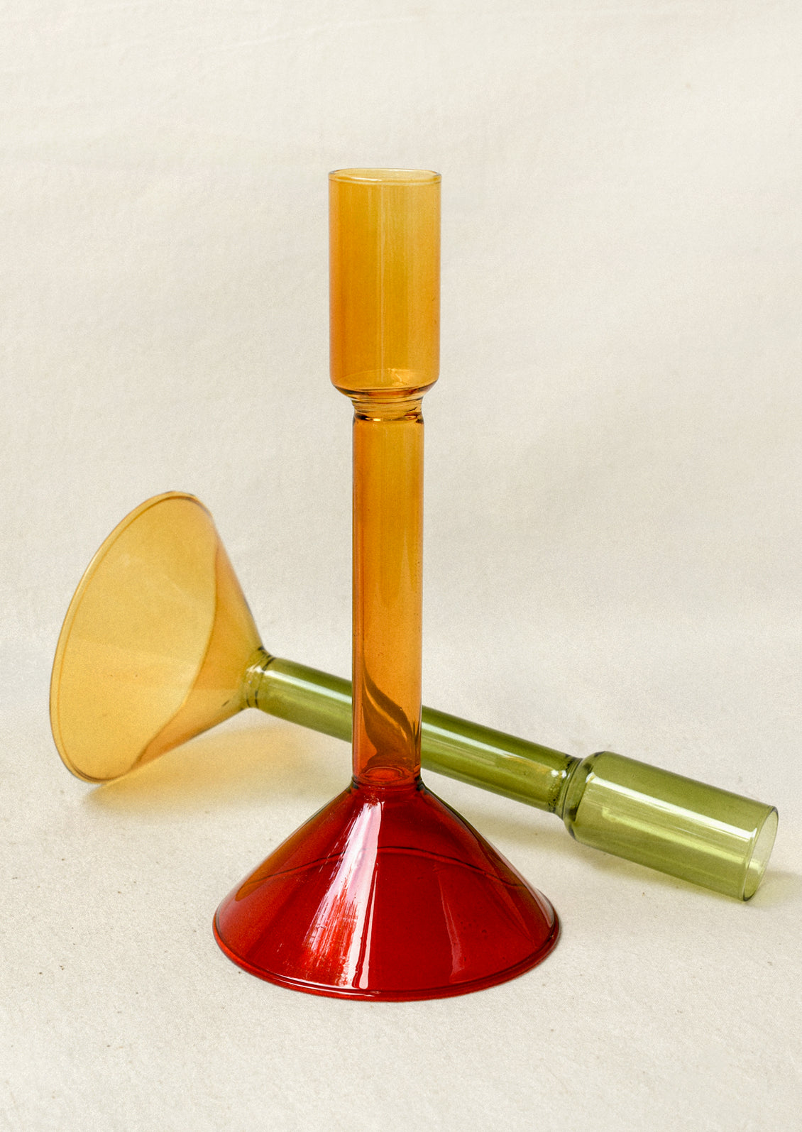 Two two-tone glass taper holders: one that is yellow and red and another that is green and yellow.
