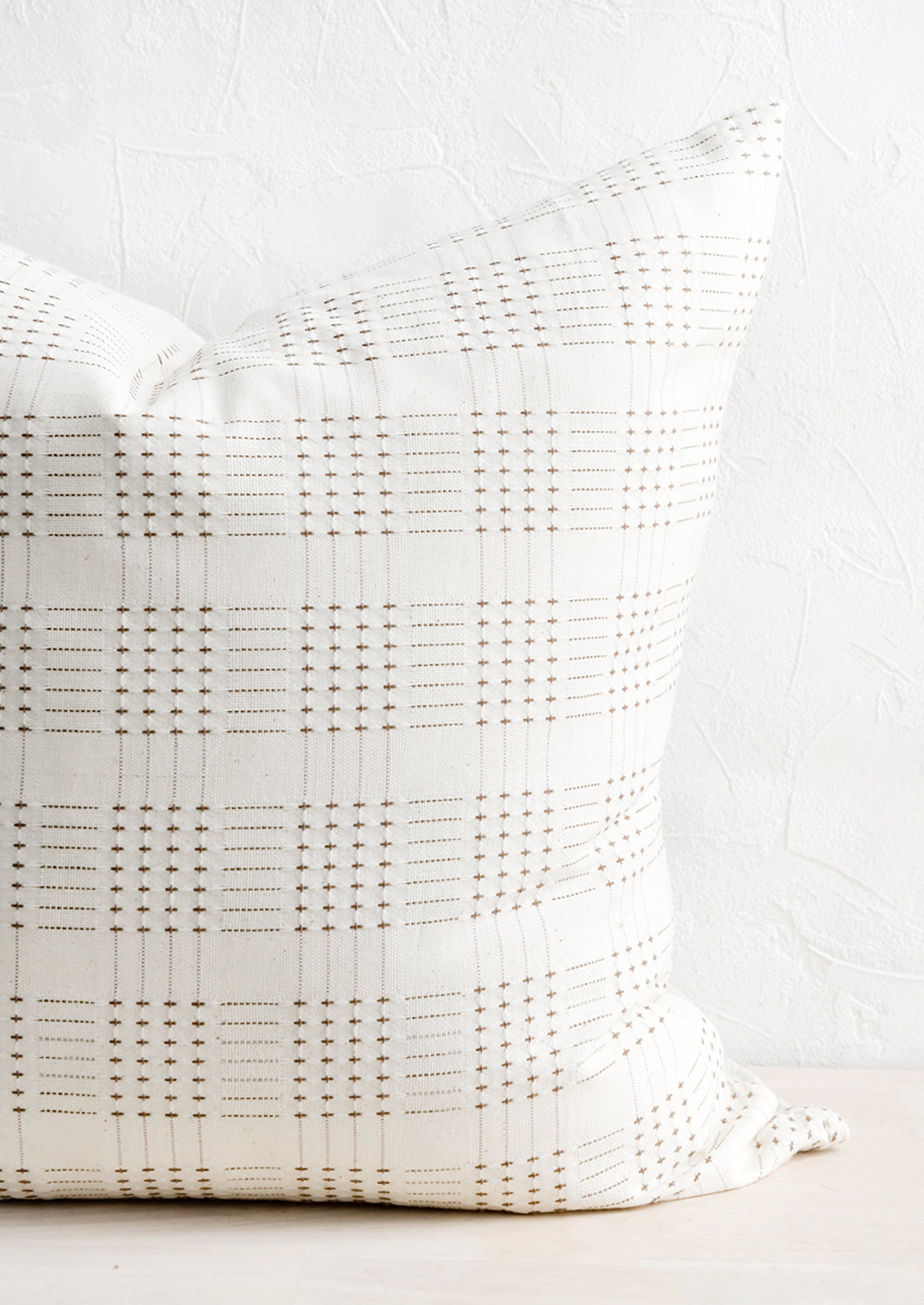 A natural cotton throw pillow with embroidered basketweave pattern in brown.