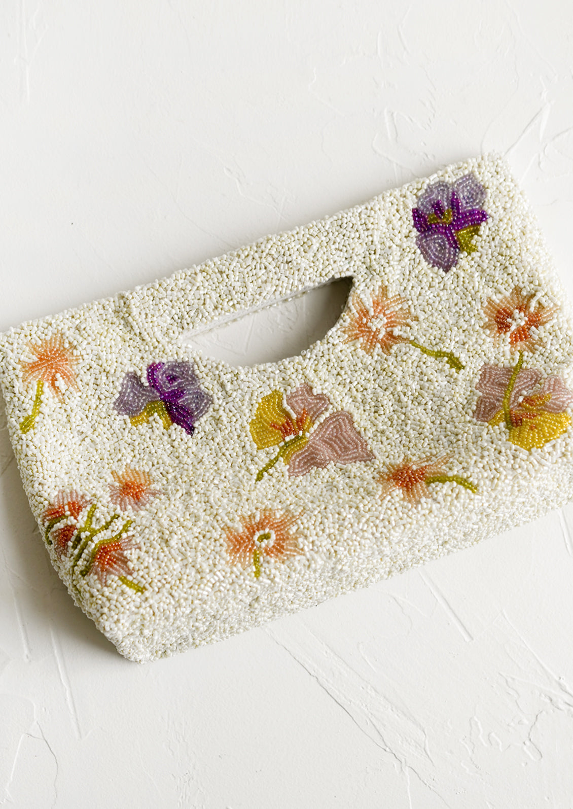 A white beaded east-west clutch with cutout handle and pastel floral pattern.