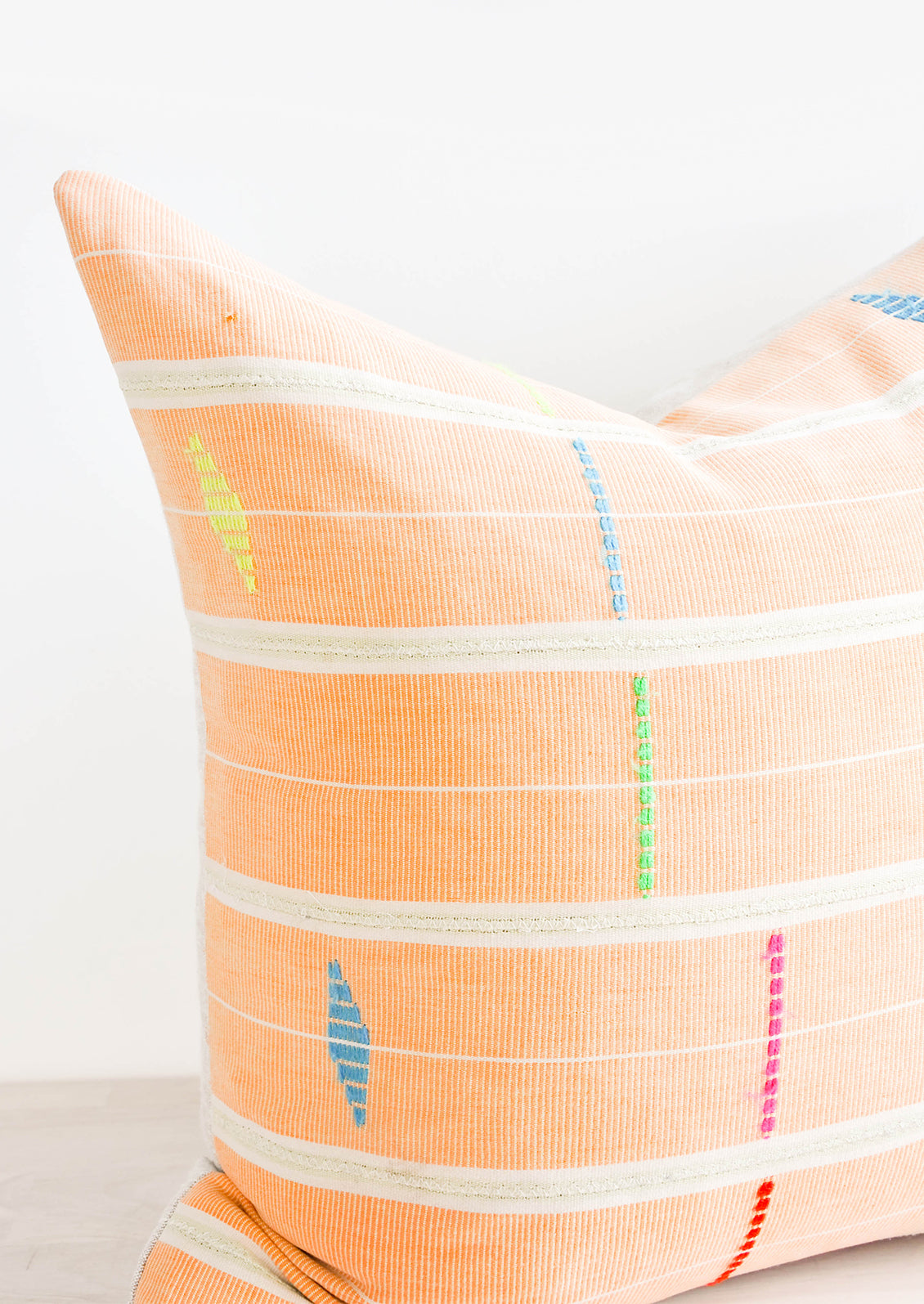 Close up of Square throw pillow made from vintage African fabric in bright orange with neon embroidery details.
