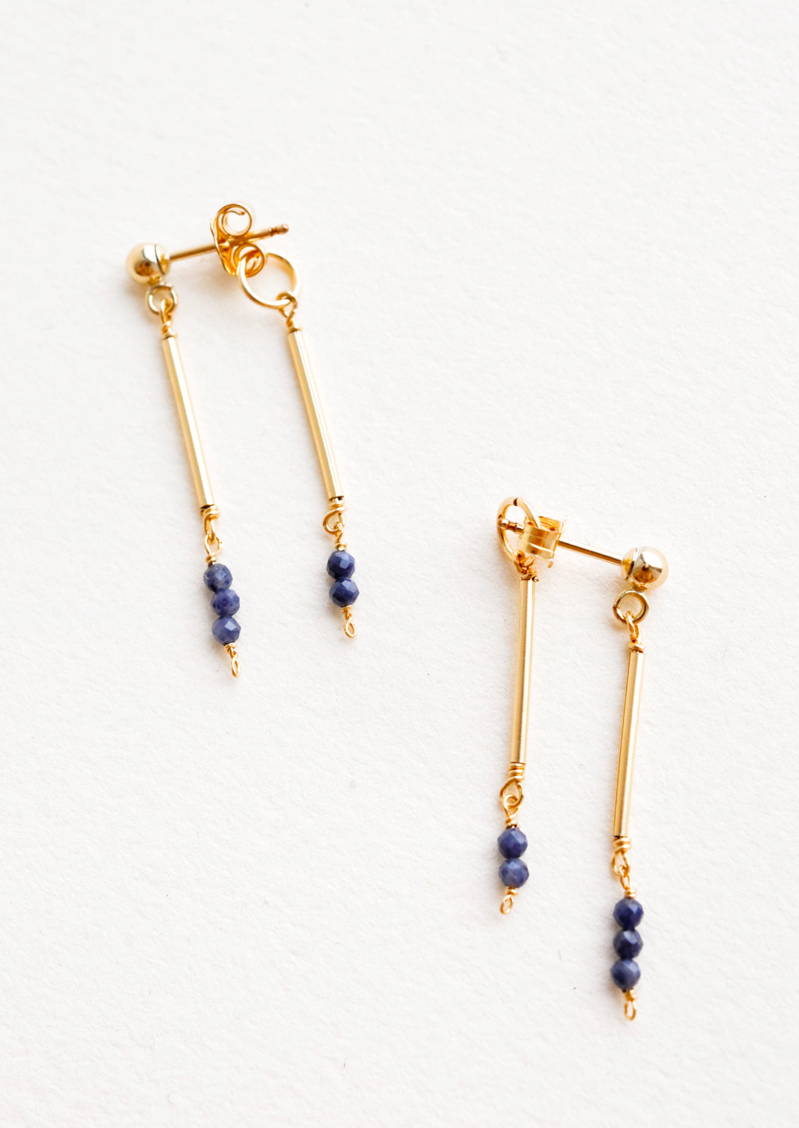 Two part dangling earrings featuring gold post and blue beads hanging from each of the post and the earring back.