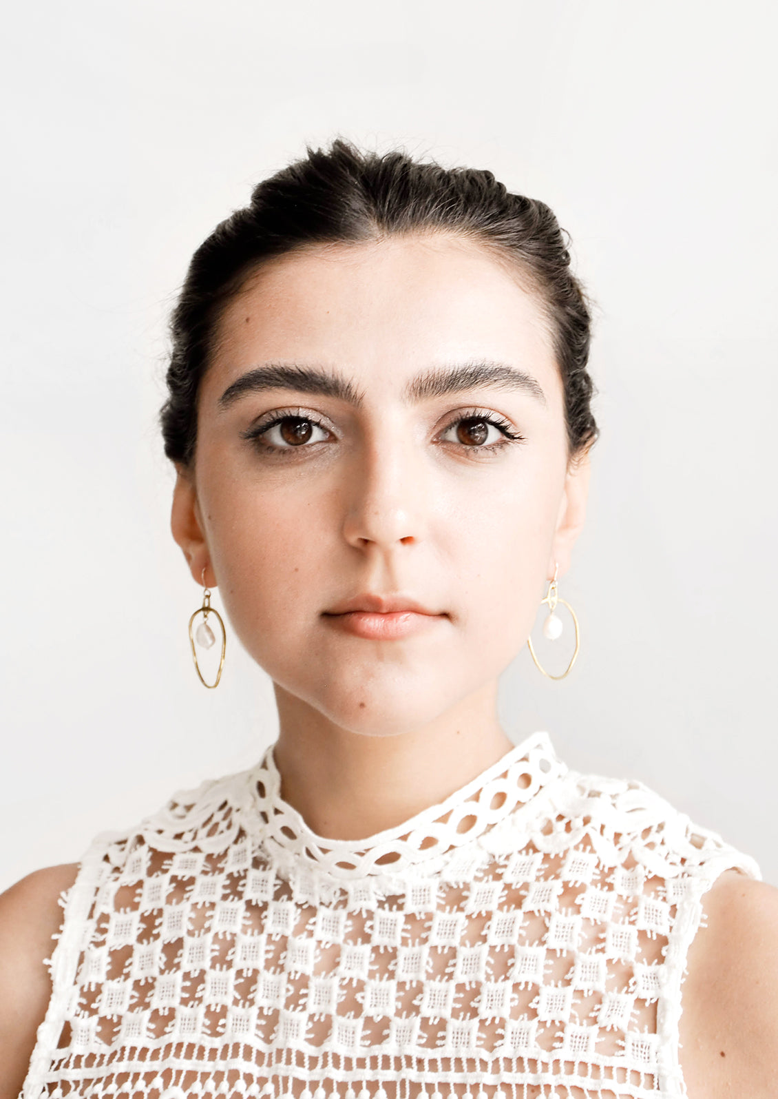 Model wears circular gold earrings with pearl.