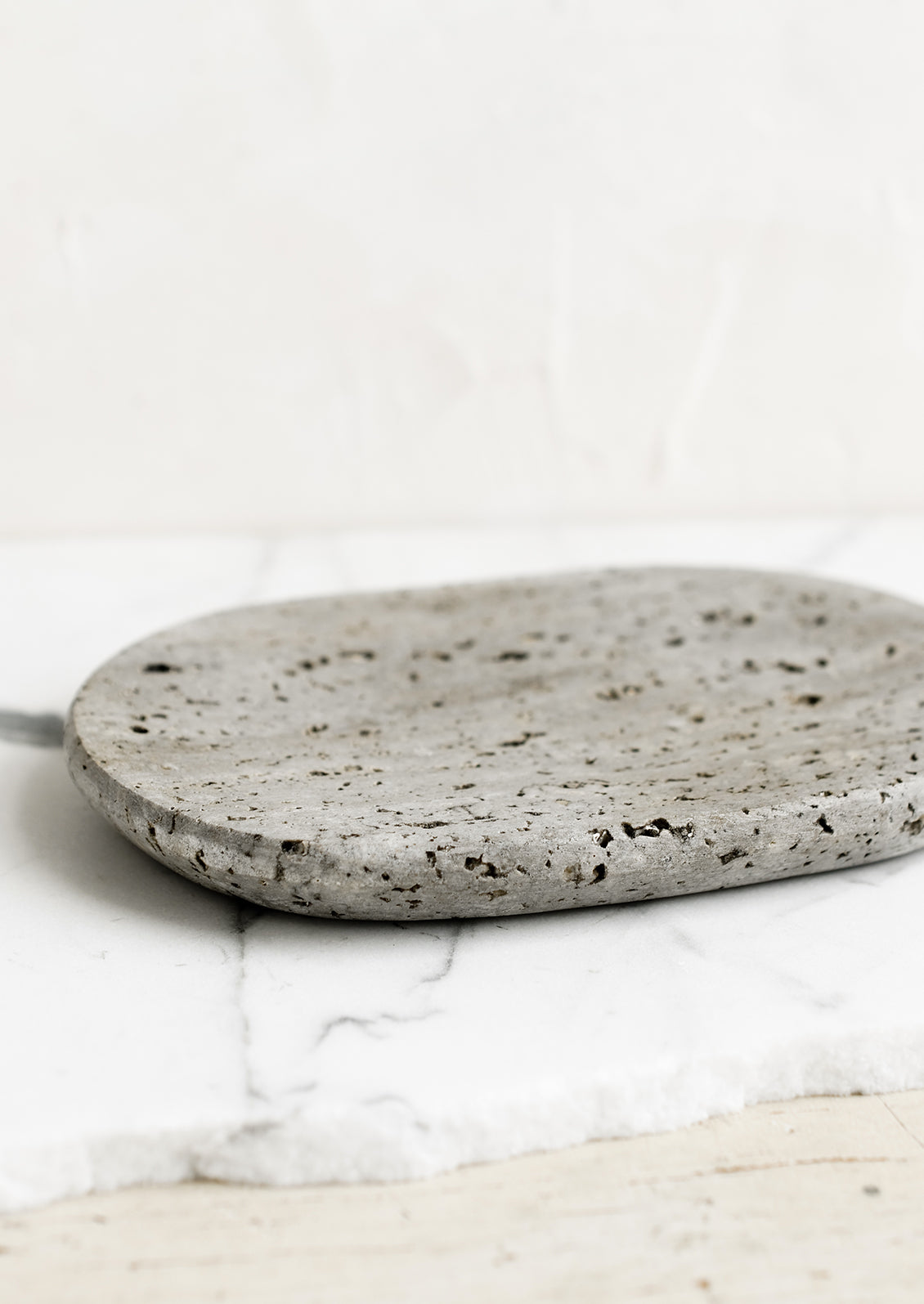 An oval-shaped soap dish in grey travertine.