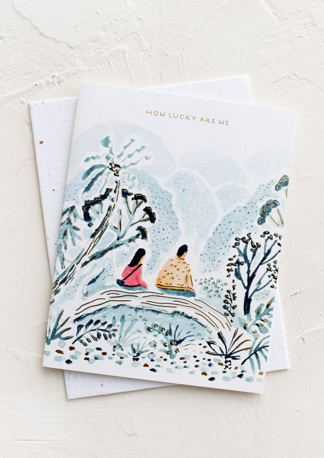 A greeting card with image of couple sitting on a bridge, text above reads "How lucky are we".