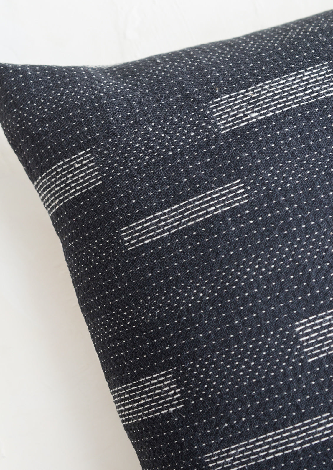 Square pillow in black with white variegated stitching in assorted line patterns