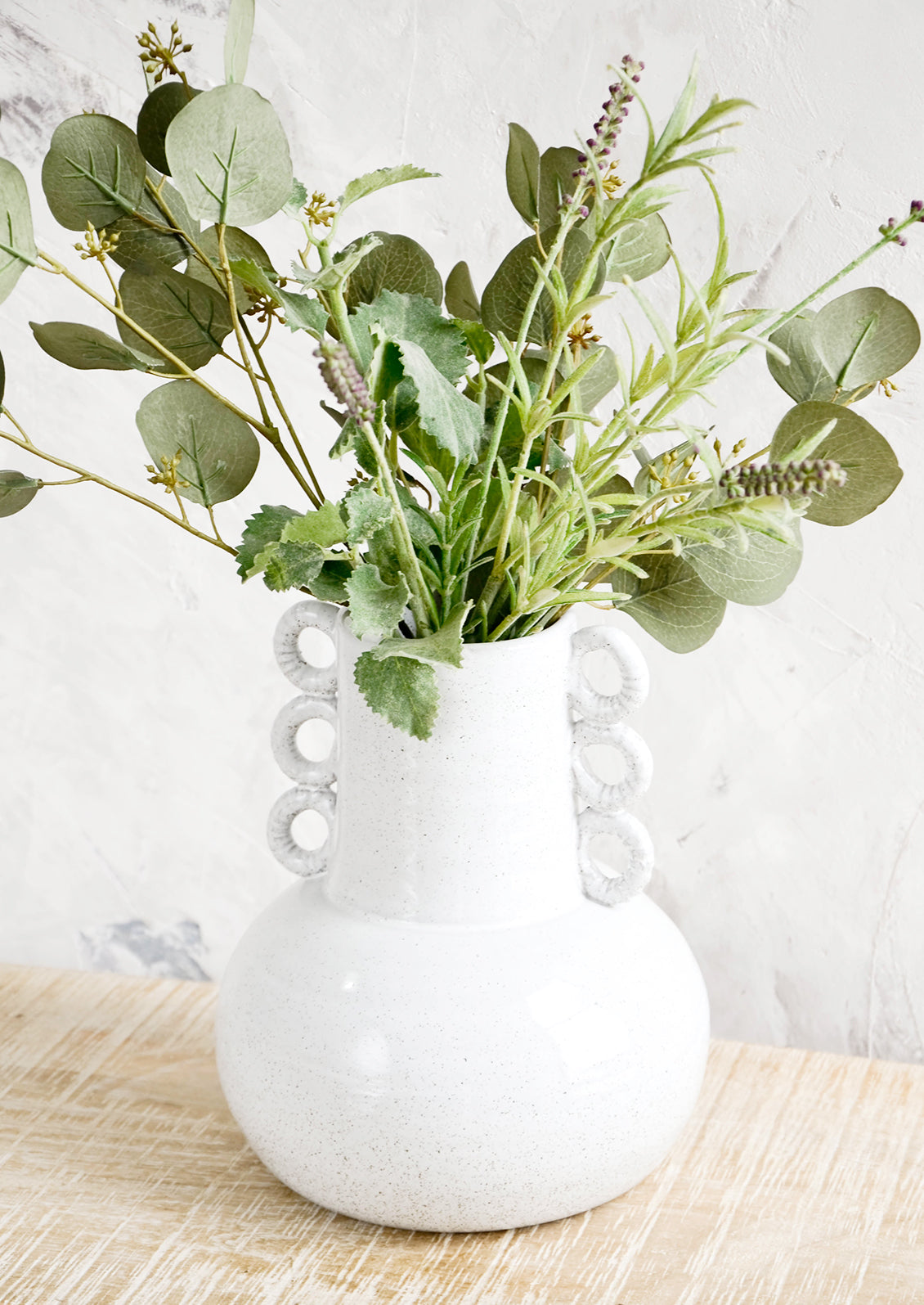 Large sculptural white ceramic vase on a rustic table with a mix of herbs & eucalyptus