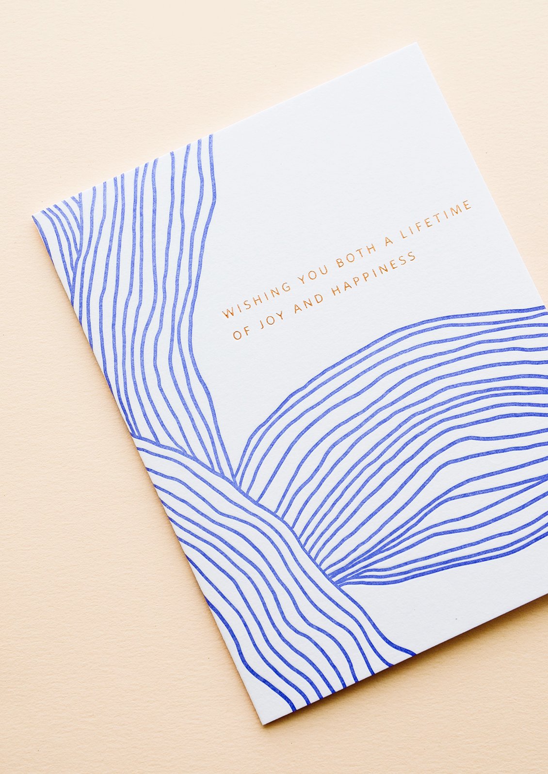 Greeting card with wavy cobalt blue line pattern and gold text reading "Wishing you both a lifetime of happiness"