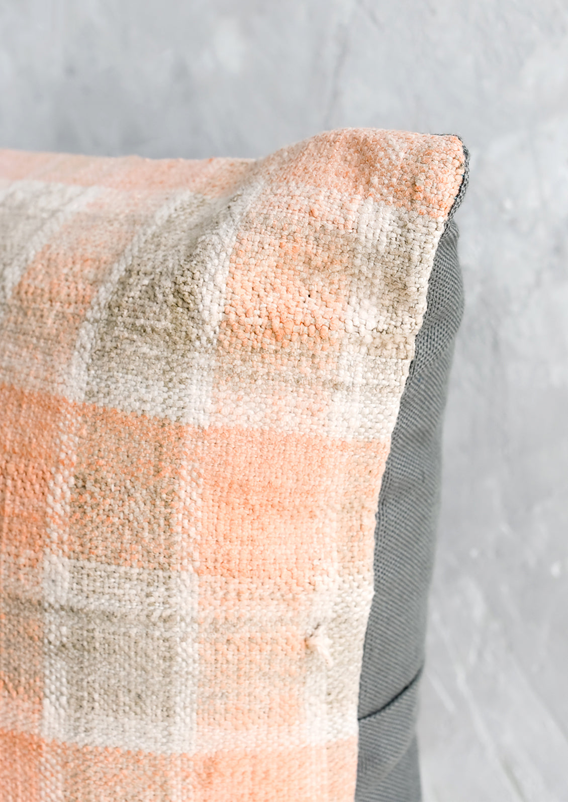 A square kilim throw pillow in peach and grey gingham with grey canvas backing.