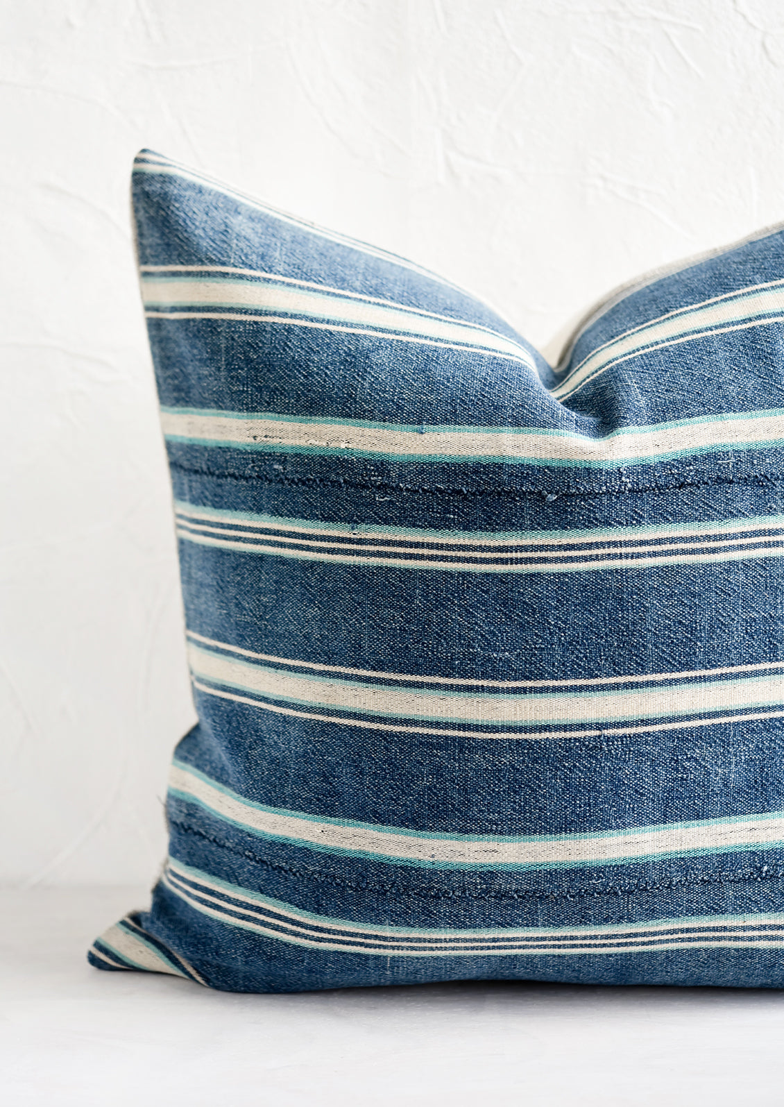 A square throw pillow in vintage indigo stripe fabric.