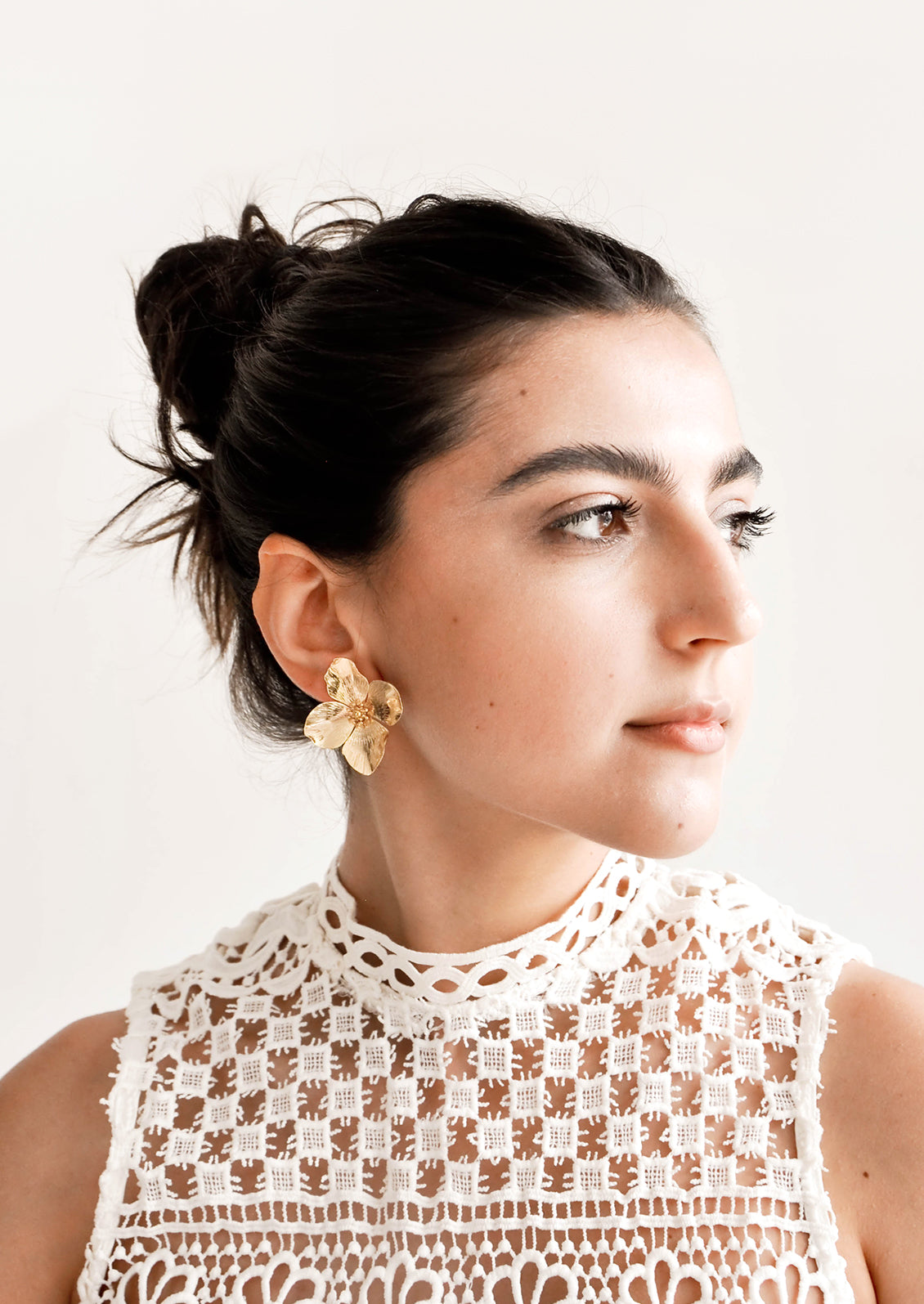 Model wears gold flower-shaped earrings and white top.