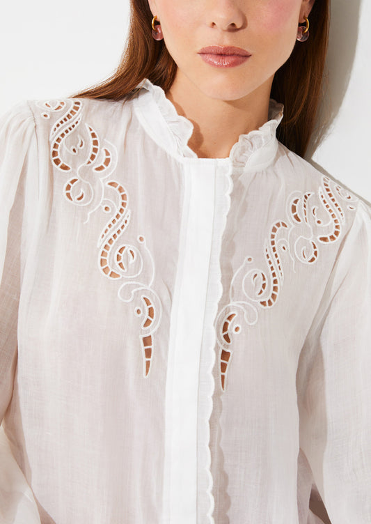 A woman wearing a white linen blouse with ruffled collar and cutwork embroidery detailing.