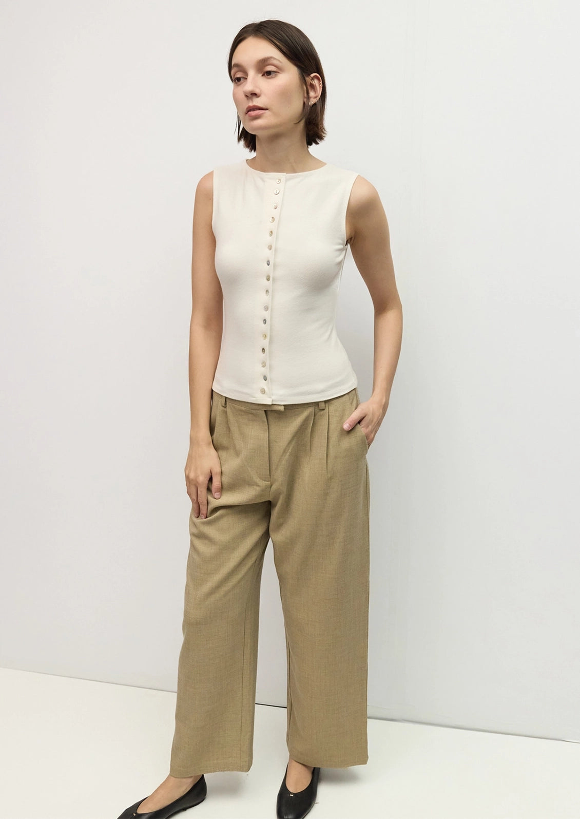 A person wearing a high neck sleeveless top in cream with mixed button front.