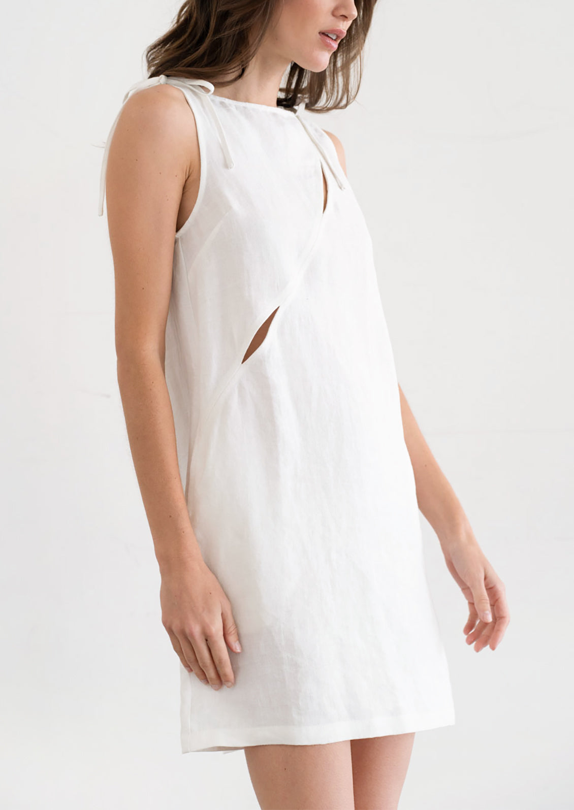 A person wearing an A-line mini dress in white with diagonal slit detail across chest.