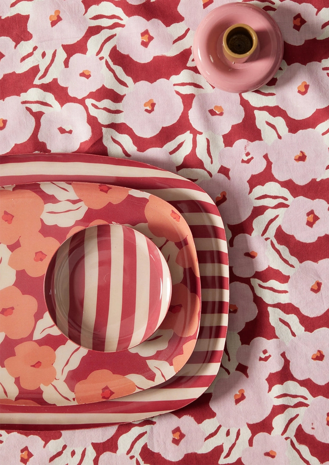 A styled flat-lay of pink and white patterned tableware, including a rectangular tray, a round plate, and a small pink cup, arranged on a matching floral fabric background.