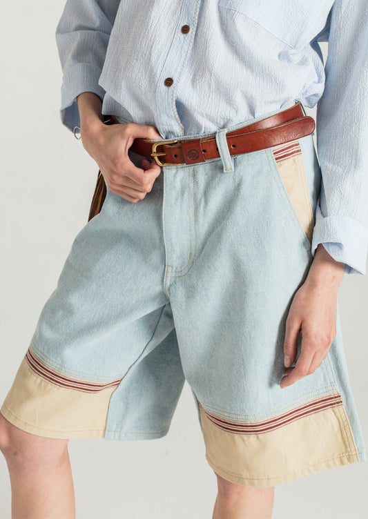 A woman wearing a pair of light denim bermuda shorts with contrast fabric at front hem.