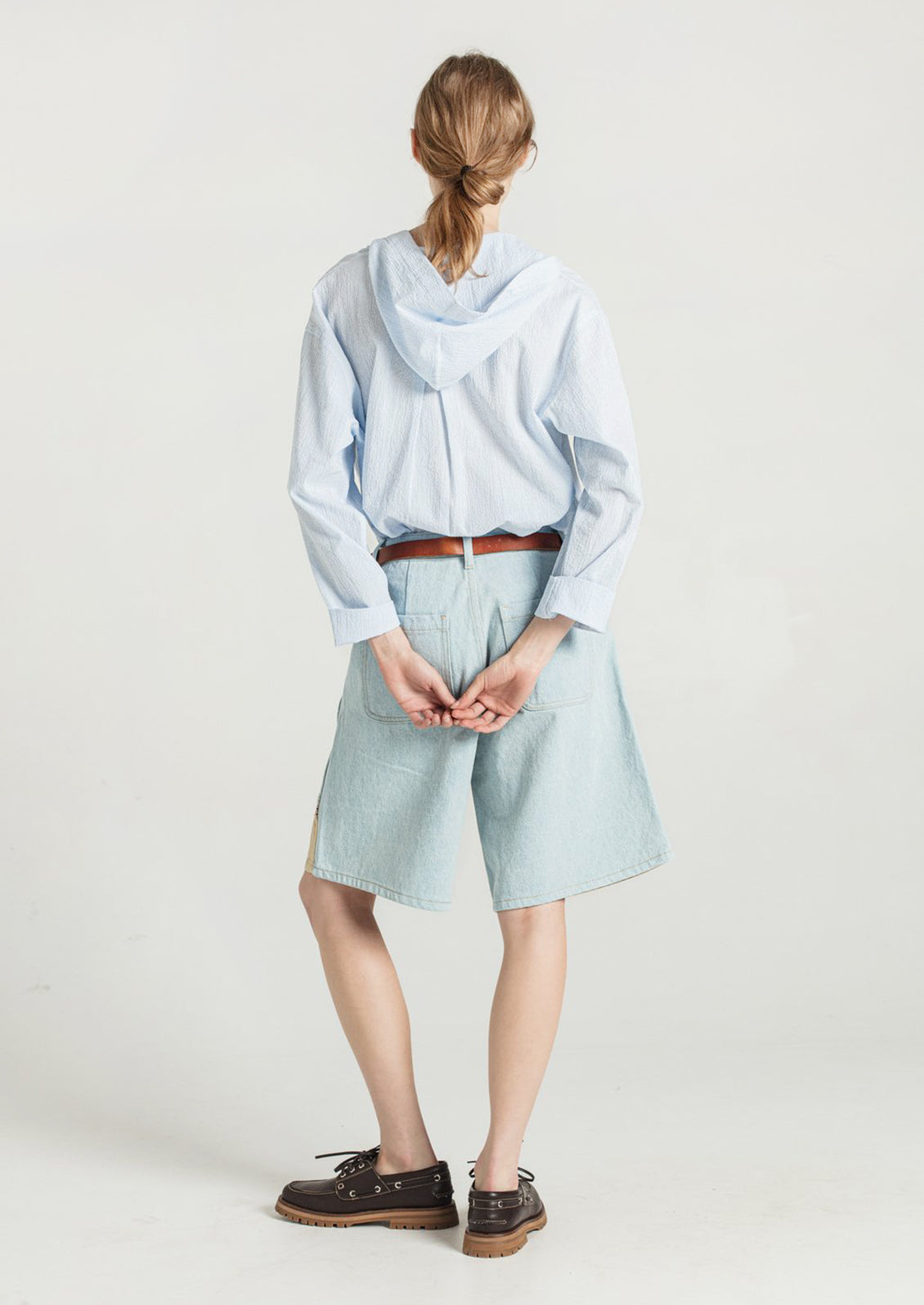 A woman wearing a pair of light denim bermuda shorts with contrast fabric at front hem.