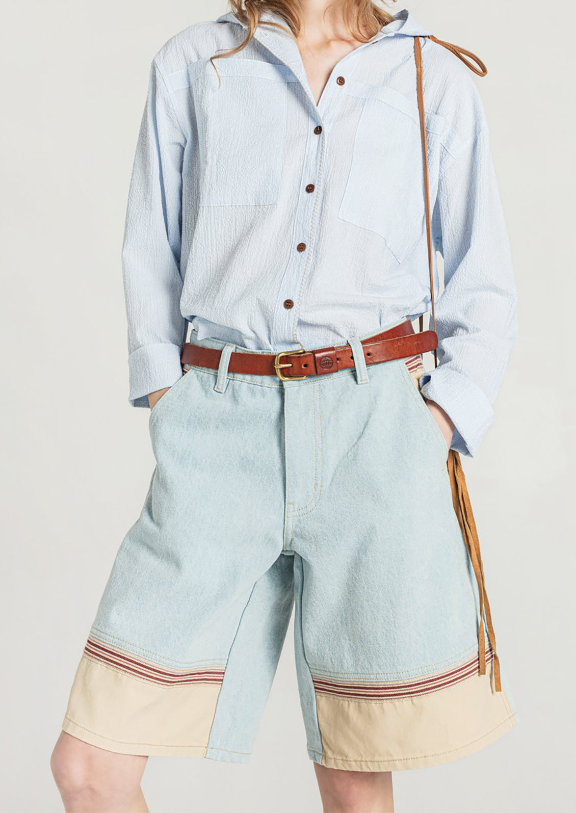 A woman wearing a pair of light denim bermuda shorts with contrast fabric at front hem.