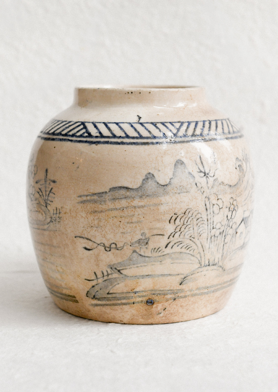 An aged stoneware ginger jar in beige patina with scenic scene in blue.