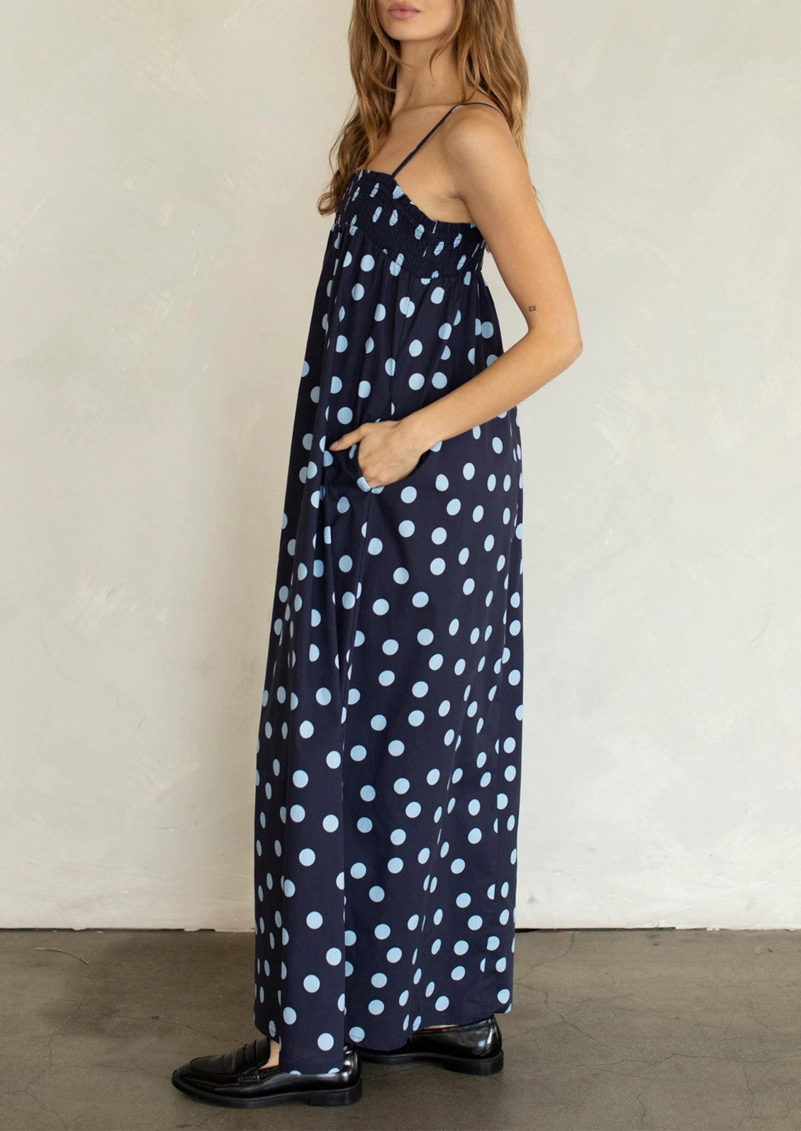 Woman wearing a navy blue dress with white polka dots against a plain background