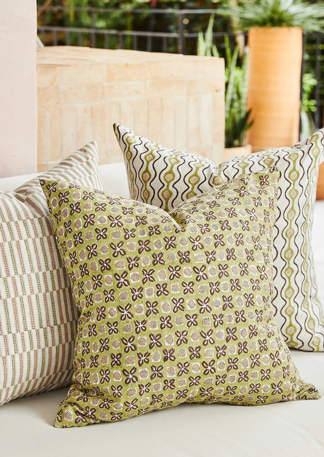 Three decorative throw pillows arranged on a light-colored outdoor sofa. The front pillow is olive green with a brown and beige geometric floral pattern.