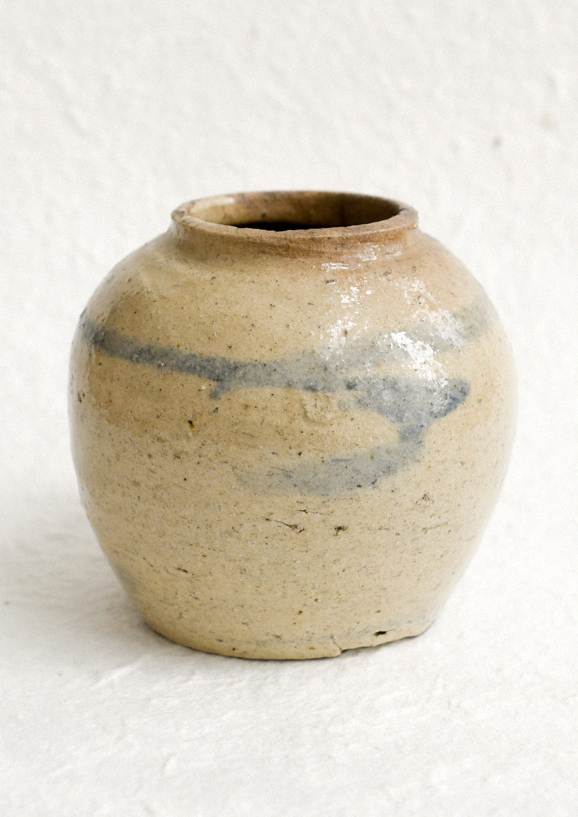 A small antique ginger jar in distressed tan ceramic with pale blue stripes.