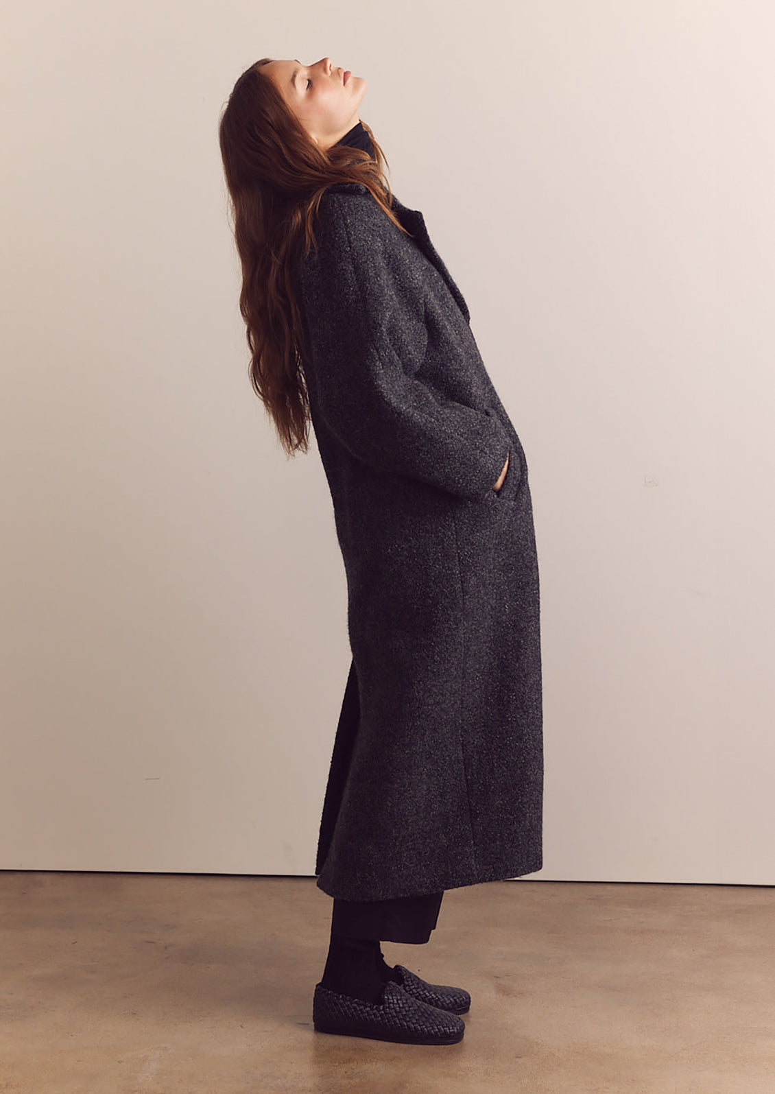 A woman wearing a long wool coat in dark grey speckled wool.