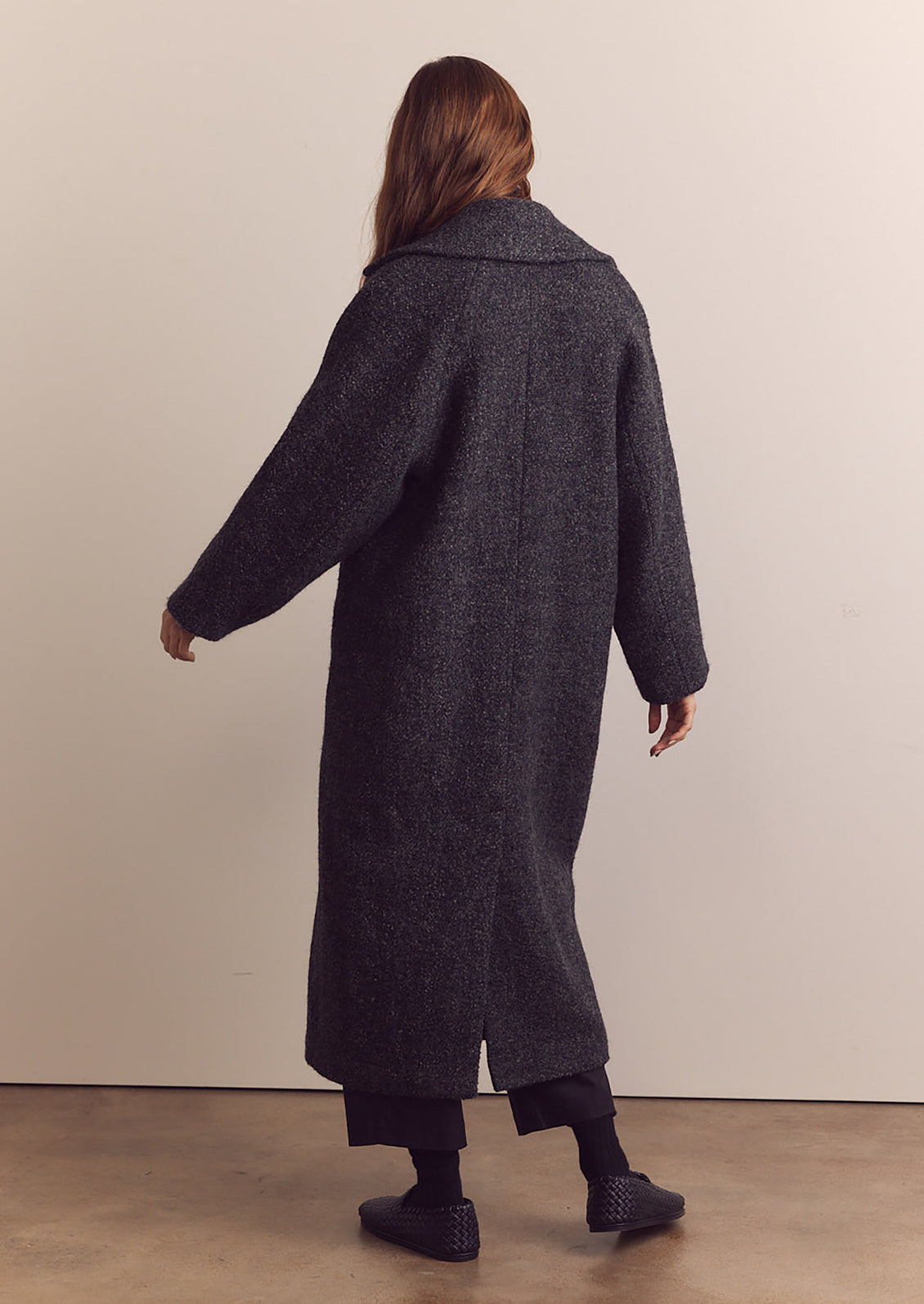 A woman wearing a long wool coat in dark grey speckled wool.