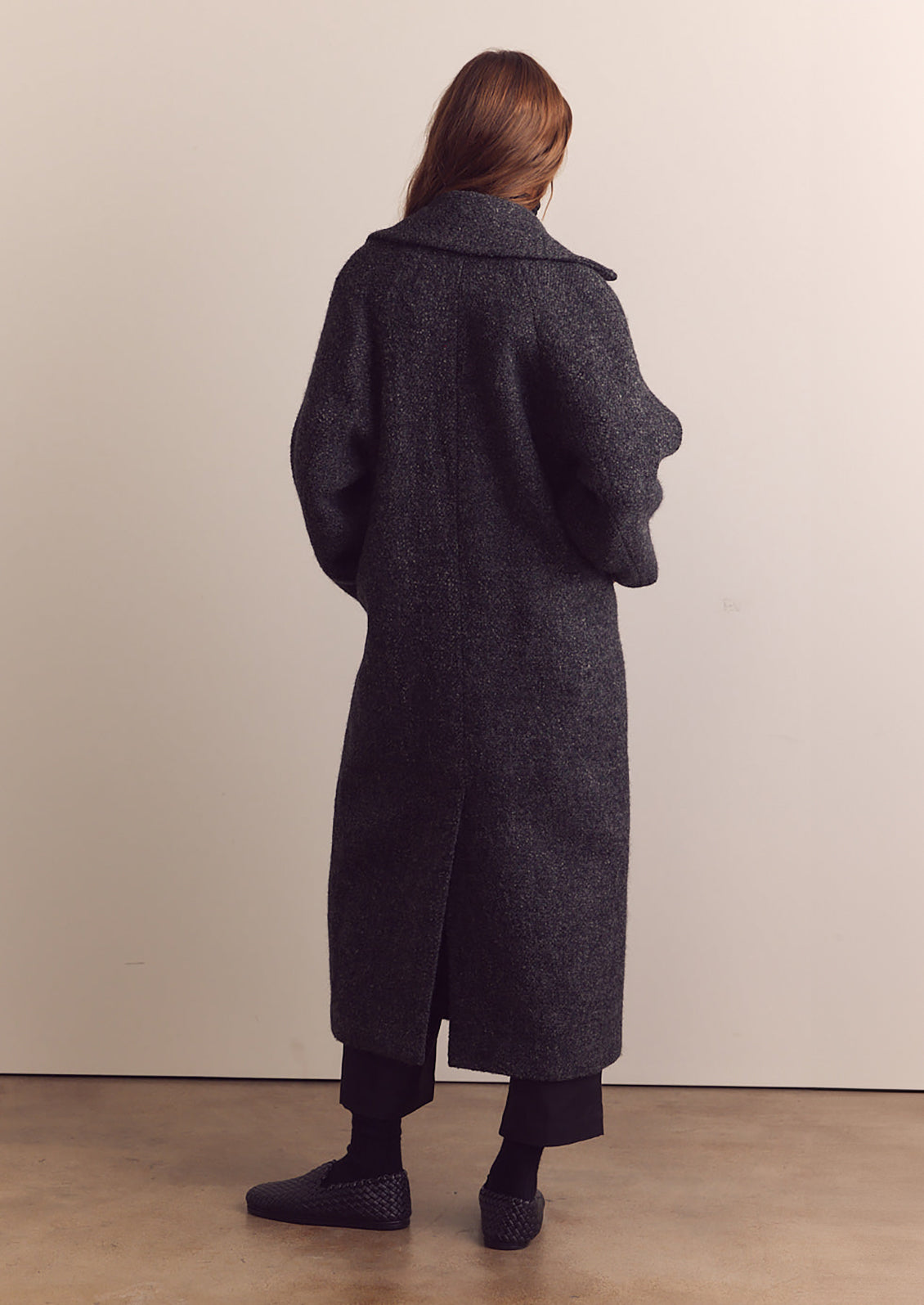 A woman wearing a long wool coat in dark grey speckled wool.
